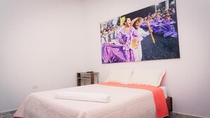 Una habitación de hotel con una cama, una mesita de noche y un cuadro en la pared que muestra un evento cultural.