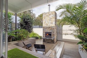 An outdoor patio with a stone fireplace, seating, and lush greenery. - Quindy Acre - Sleek Poolside Escape by Geographe Bay (Dunsborough)