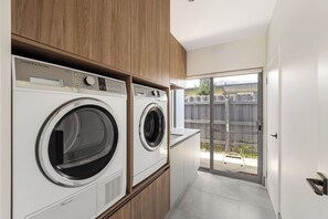 A laundry room with two front-loading washing machines, wooden cabinets, and a sliding glass door leading to an outdoor area. - Quindy Acre - Sleek Poolside Escape by Geographe Bay (Dunsborough)