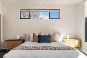 A bedroom with a large bed, two nightstands, a window with blinds, and a view of trees. - Quindy Acre - Sleek Poolside Escape by Geographe Bay (Dunsborough)