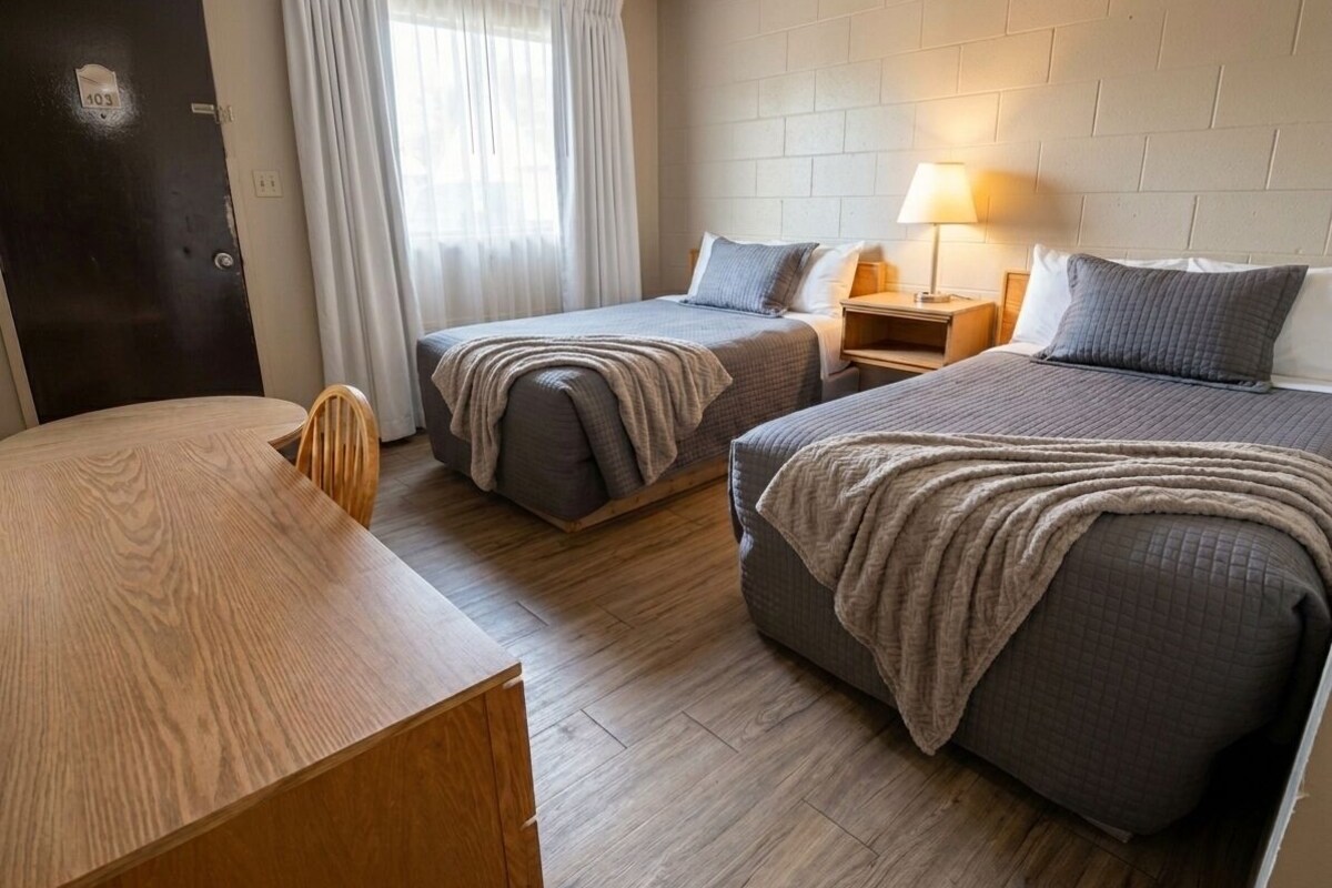 Ein Hotelzimmer mit zwei Betten, einem Holztisch, einem Nachttisch mit Lampe und einer Tür mit der Nummer 403.