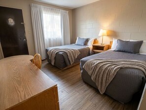 Ein Hotelzimmer mit zwei Betten, einem Holztisch, einem Nachttisch mit Lampe und einer Tür mit der Nummer 403.