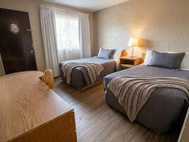 Una habitación de hotel con dos camas, un escritorio de madera, una mesita de noche con lámpara y una puerta con el número 403.