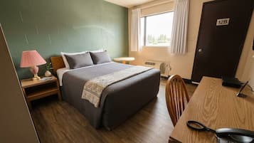 A hotel room with a bed, bedside table, lamp, desk with a telephone, and a door labeled '12B'.