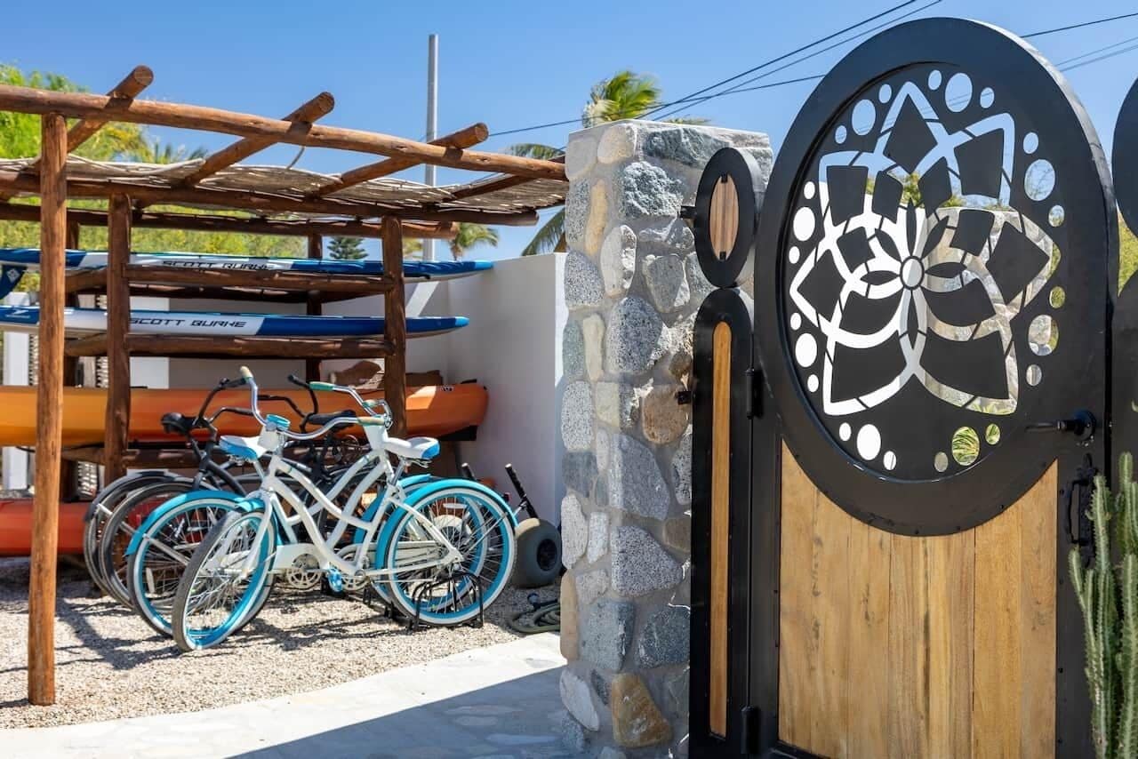 En grind med en mur av sten och en trädörr, ett cykelställ med cyklar och en pergola av trä.