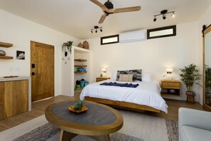 Ein Schlafzimmer mit einem Bett, Nachttischen, einem Deckenventilator, einem runden Tisch und einer Topfpflanze.