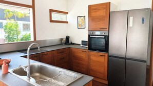 A modern kitchen with a stainless steel sink, wooden cabinets, a built-in oven, and a refrigerator.