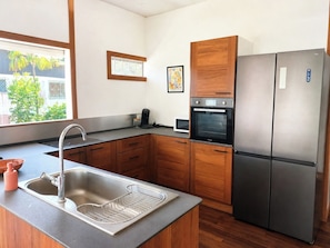 A modern kitchen with a stainless steel sink, wooden cabinets, a built-in oven, and a refrigerator.