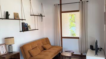 Ein modernes Wohnzimmer mit einer Couch, einem Deckenventilator, einem Fernseher und einem Fenster mit Vorhängen.