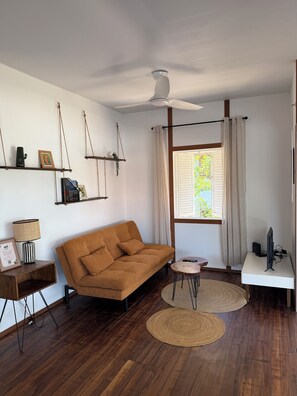 Ein modernes Wohnzimmer mit einer Couch, einem Deckenventilator, einem Fernseher und einem Fenster mit Vorhängen.