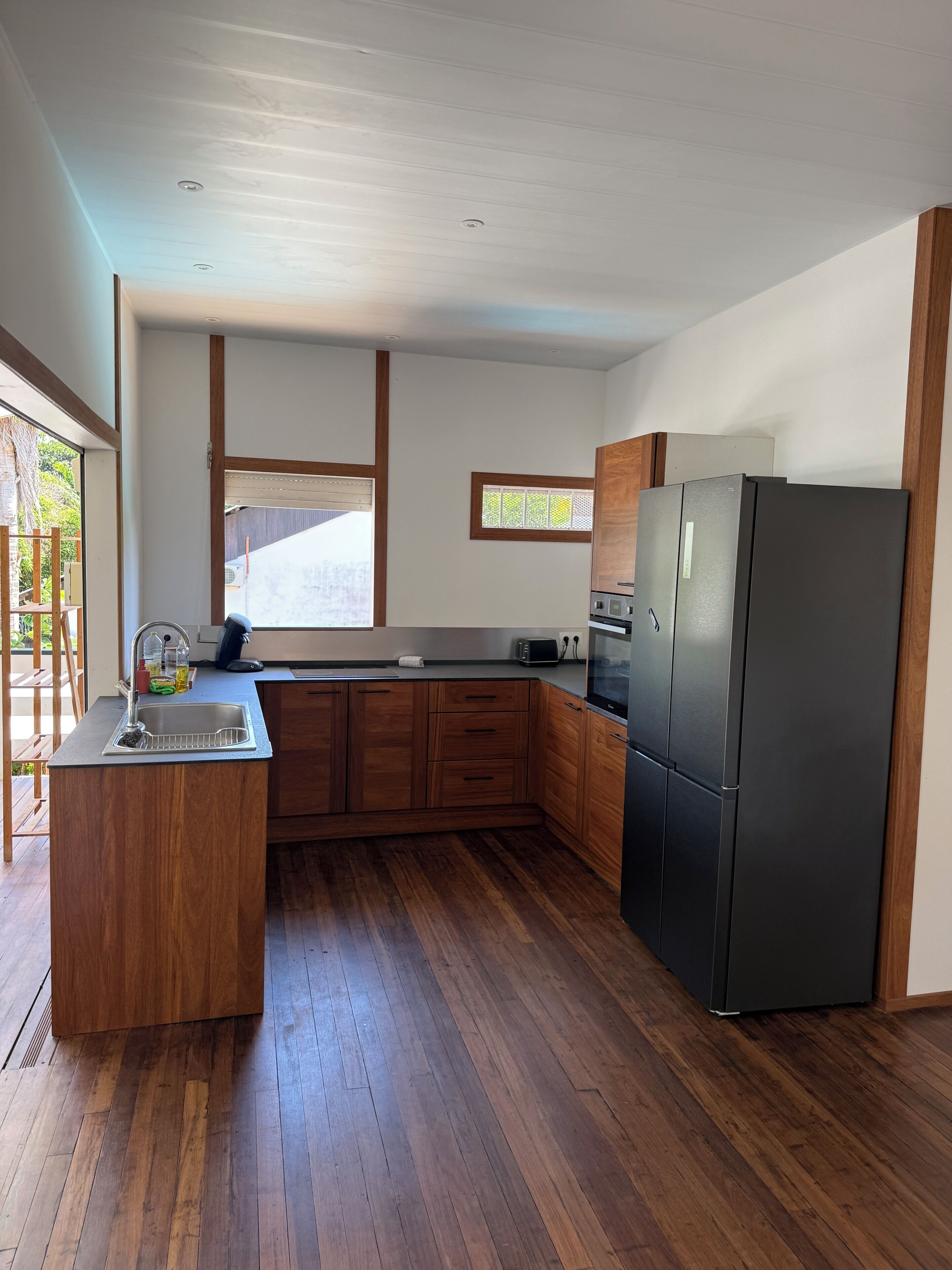 A modern kitchen with wooden cabinets, a black refrigerator, and a window with blinds.
