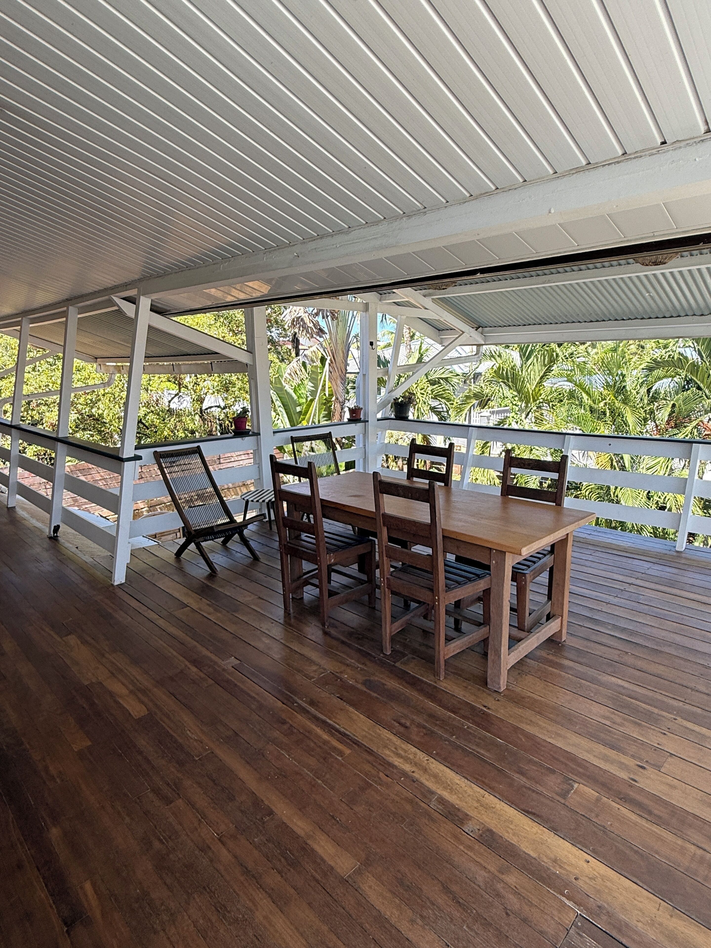 An outdoor wooden deck with a table and chairs, surrounded by a white railing, overlooking a lush green landscape.