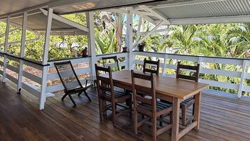 An outdoor wooden deck with a table and chairs, surrounded by a white railing, overlooking a lush green landscape.