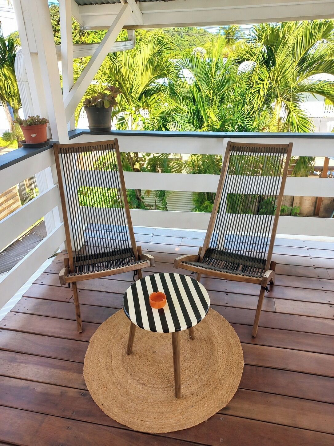 Deux chaises en bois, dotées de coussins à rayures noires et blanches, sont posées sur une terrasse en bois, devant laquelle se trouve un tapis tissé.