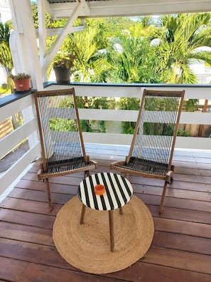 Two wooden chairs with black and white striped cushions on a wooden deck, with a woven mat in front.