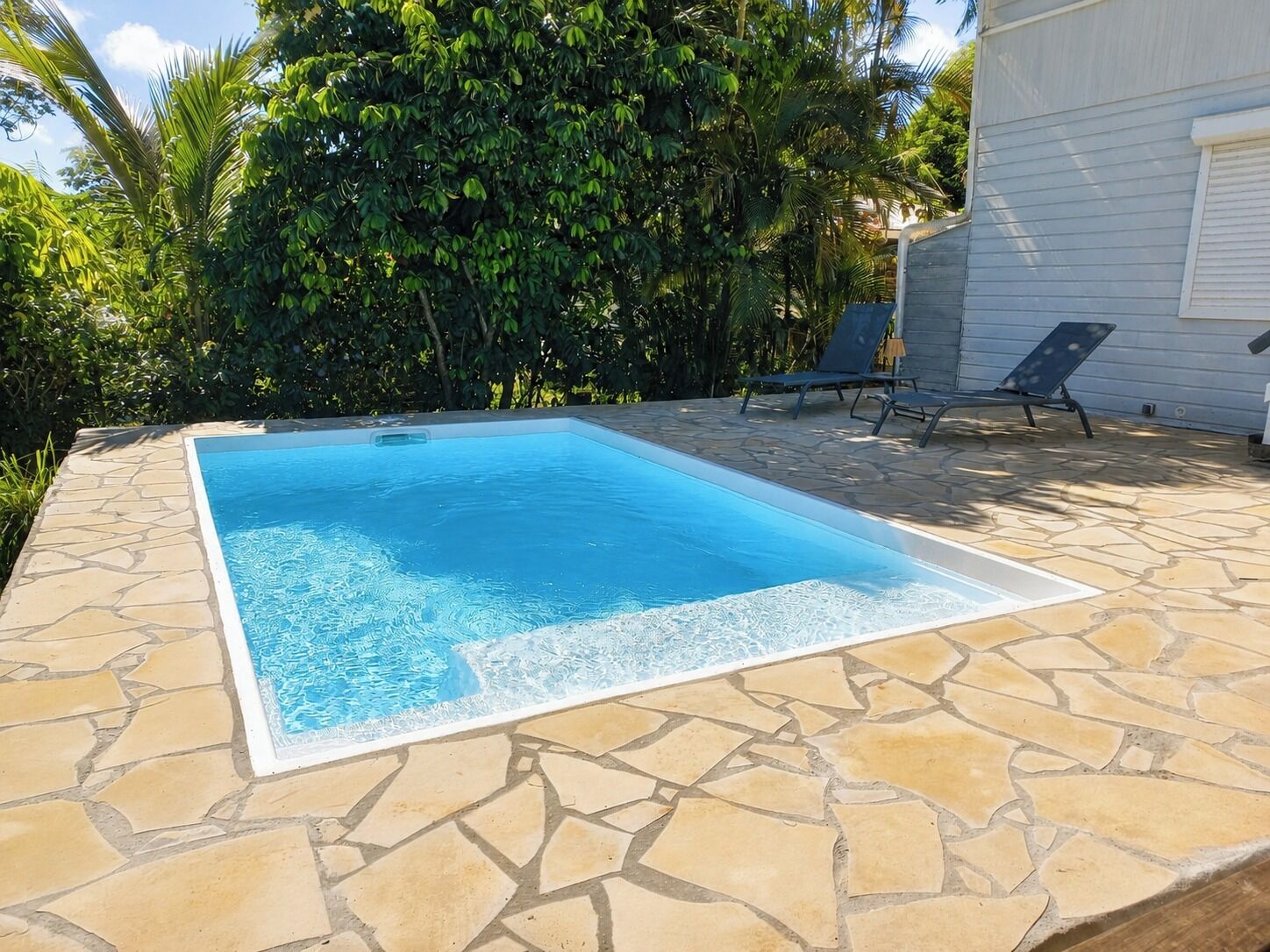 Une piscine rectangulaire bordée de pierres, entourée d’une terrasse aménagée avec des chaises longues.