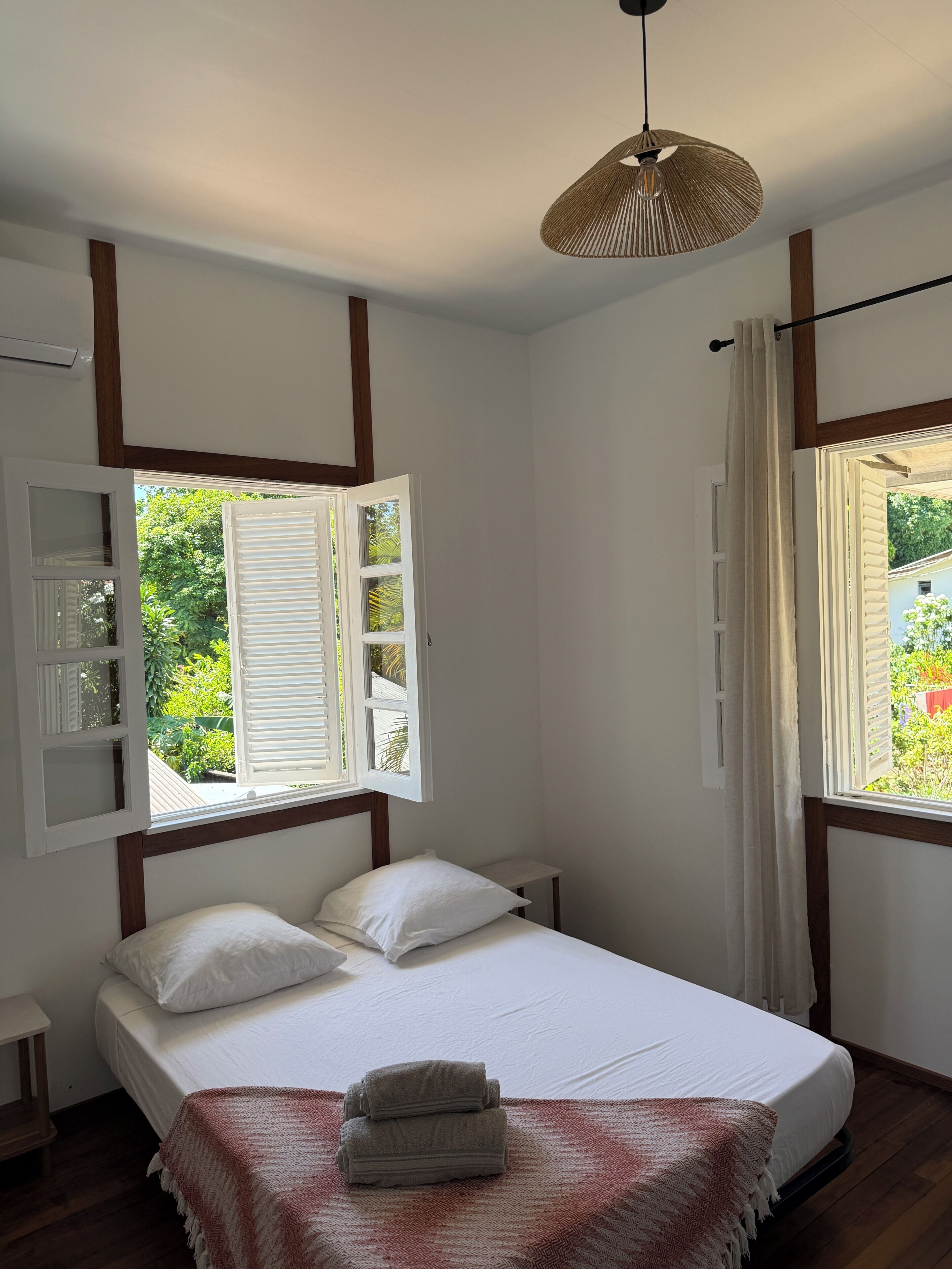 Een slaapkamer met een bed, een nachtkastje, een hanglamp en een raam met shutters.