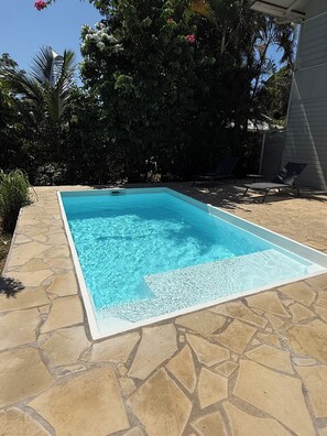 Ein rechteckiger Swimmingpool mit klarem, blauem Wasser, umgeben von einer Steinterrasse.