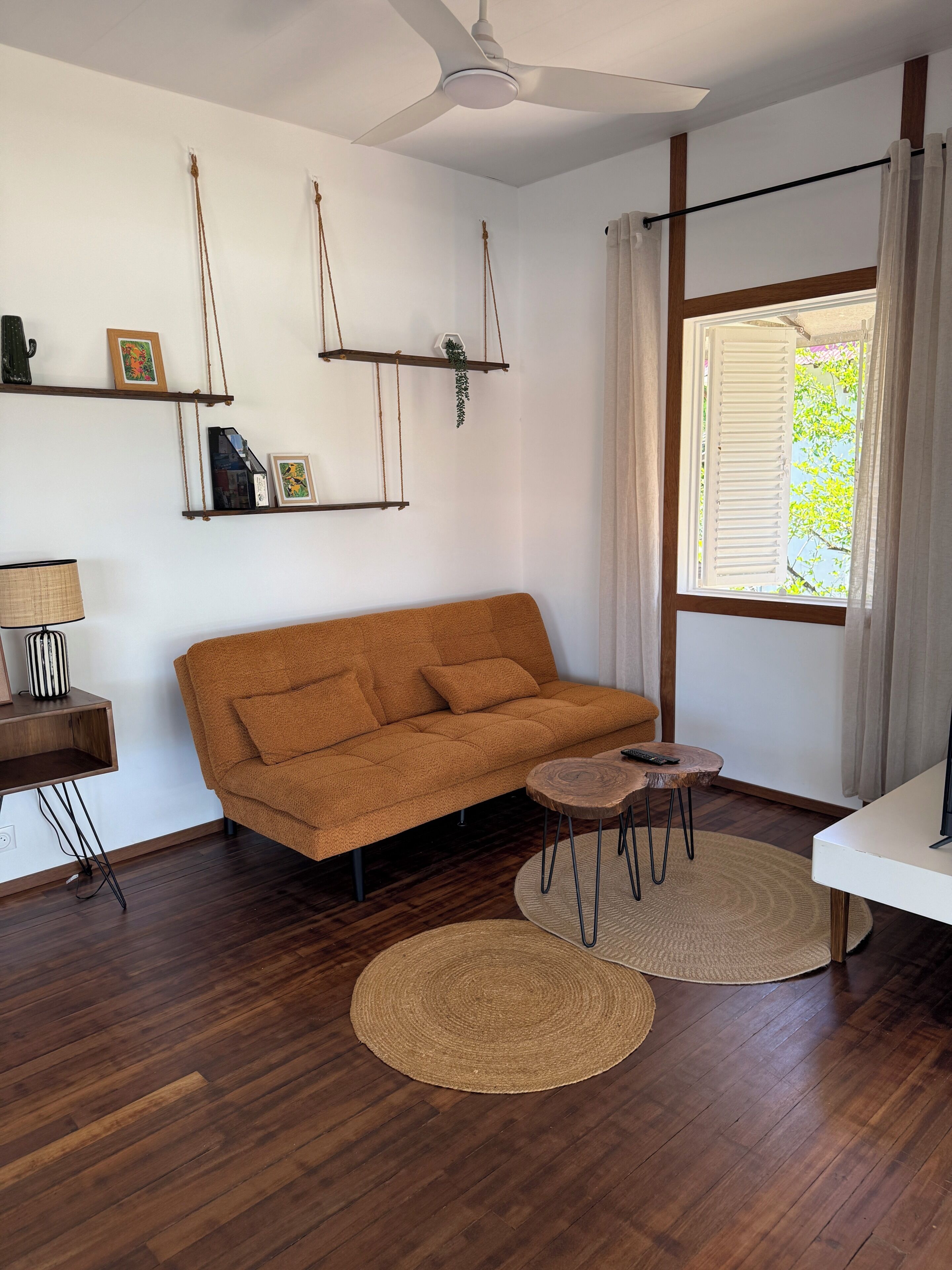 Un salon comprenant un canapé, une table basse, une lampe, un ventilateur de plafond et une fenêtre avec des rideaux.