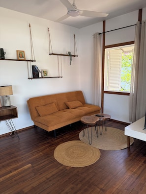 A living room with a sofa, a coffee table, a lamp, a ceiling fan, and a window with curtains.