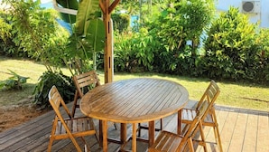 Una terraza exterior de madera con una mesa redonda y sillas, rodeada de abundante vegetación.