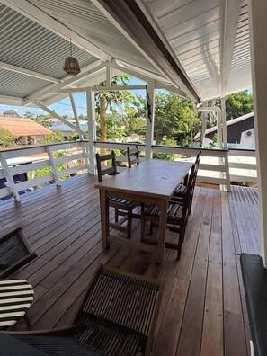 Une terrasse extérieure en bois, avec une table et des chaises, un luminaire suspendu et une vue sur les environs.