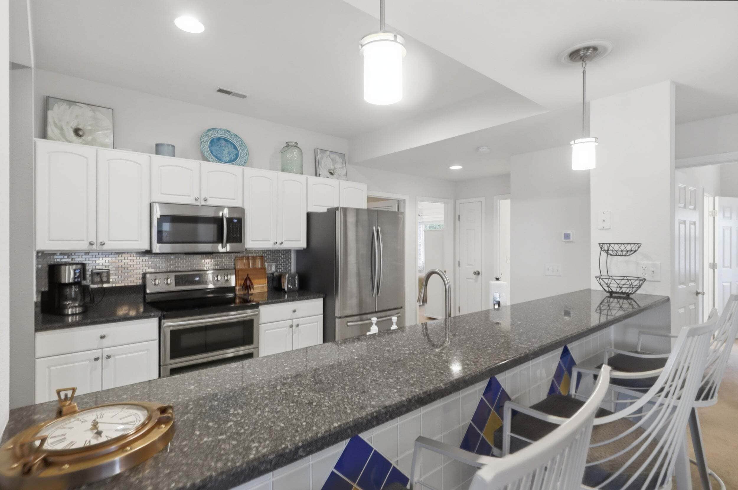 A modern kitchen with white cabinets, stainless steel appliances, a granite countertop, and a central island with bar stools.
