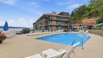 A poolside area with lounge chairs and a building with balconies.
