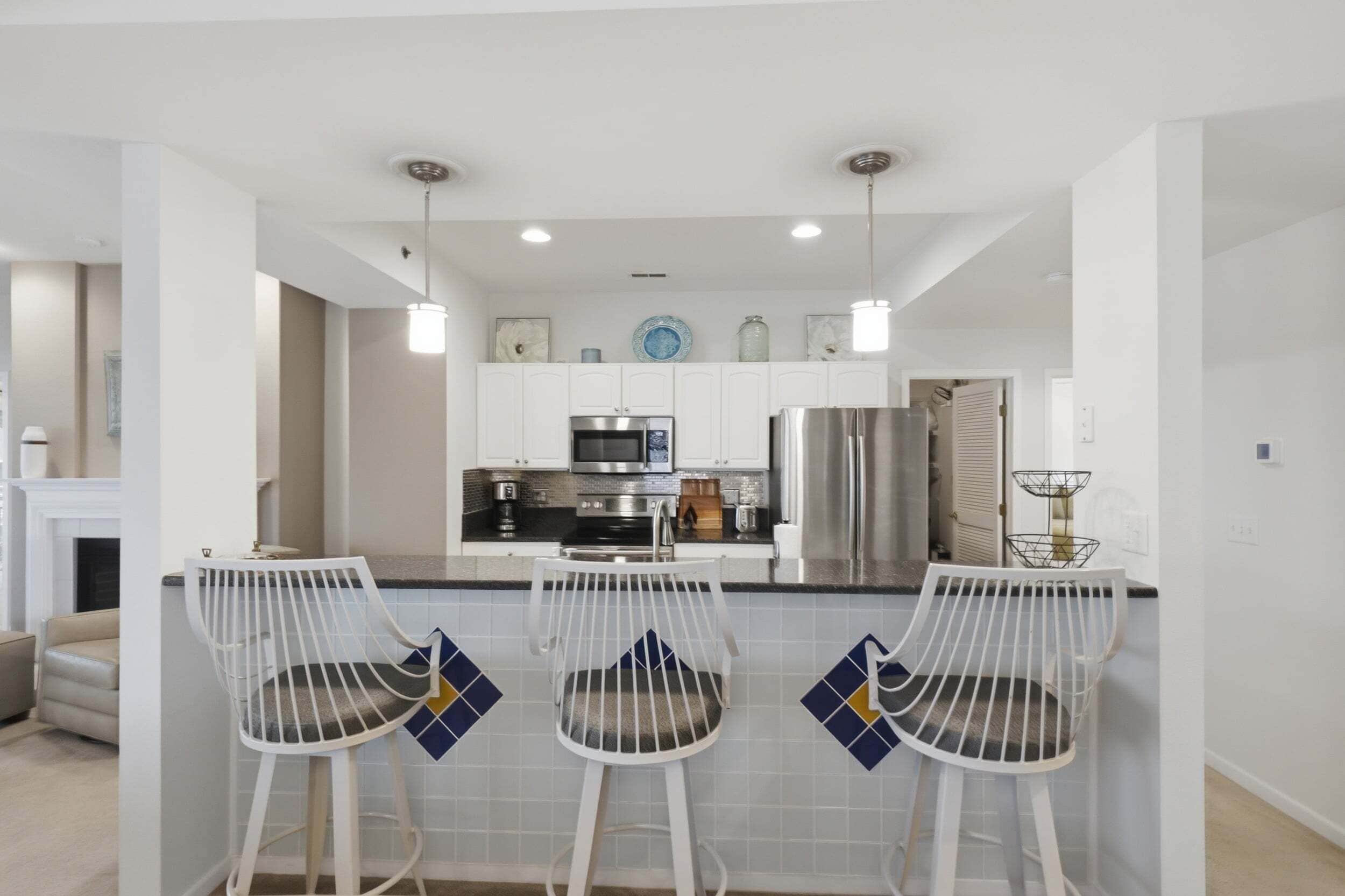 A modern kitchen with white cabinetry, stainless steel appliances, and a bar area with white bar stools.