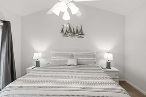 A bedroom with a bed, two bedside tables with lamps, a ceiling fan, and a wall decoration of sailboats. - Main Channel Views, 3 Heated Pools & Gated Resort (Lake Ozark)