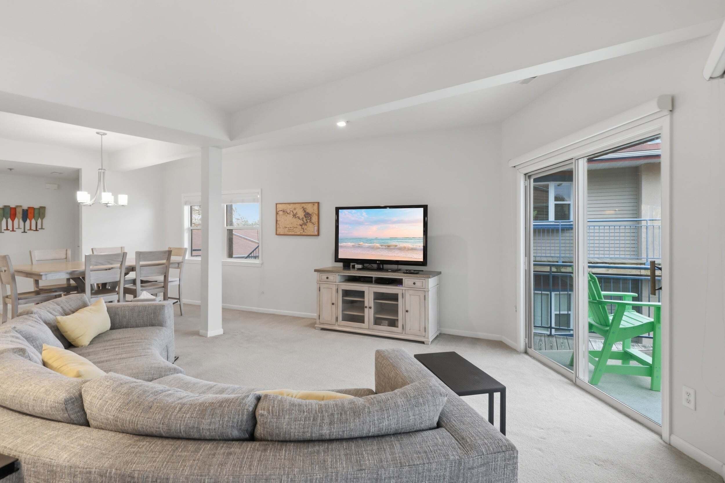A modern living room with a large L-shaped sectional sofa, a flat-screen TV, and a dining area with a wooden table and chairs.