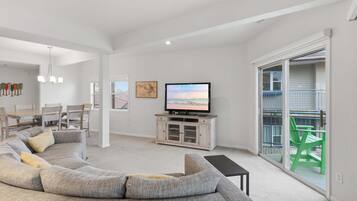 A modern living room with a large L-shaped sectional sofa, a flat-screen TV, and a dining area with a wooden table and chairs.
