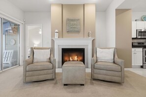 A living room with a fireplace, two armchairs, a coffee table, and a kitchen area with cabinets and appliances. - Main Channel Views, 3 Heated Pools & Gated Resort (Lake Ozark)