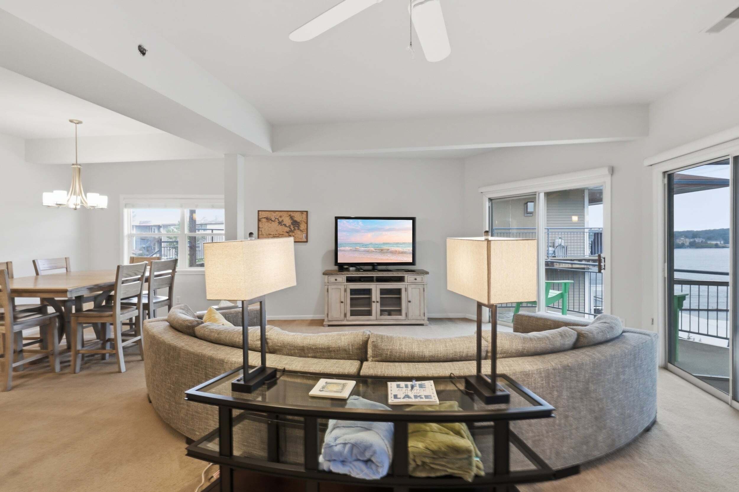 A modern living room with a curved sofa, a glass coffee table, a television, and a dining area with chairs and a table.