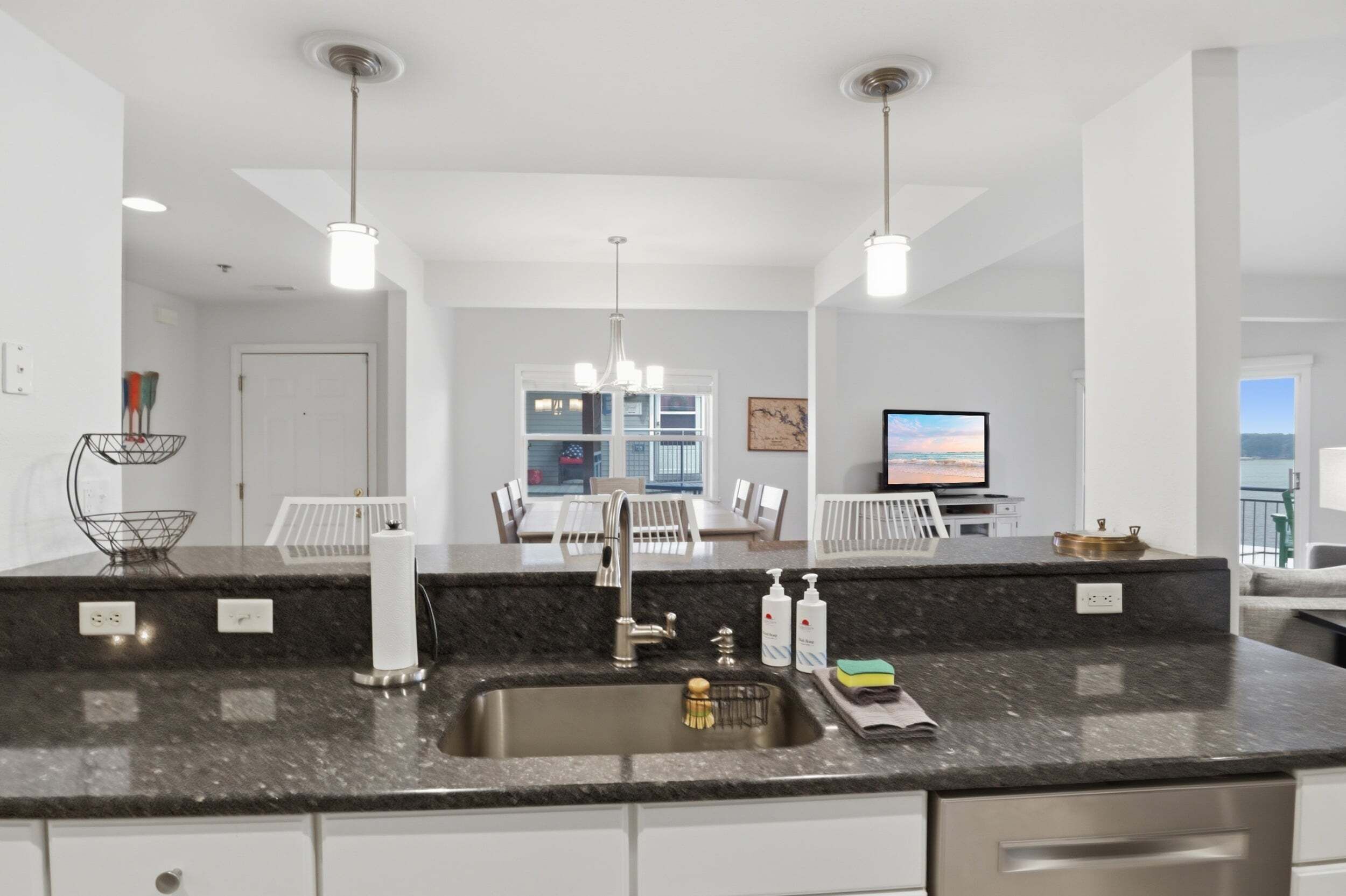A modern kitchen with a granite countertop, stainless steel sink, and pendant lighting.