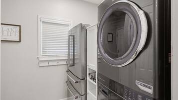 A laundry room with a front-loading washer and dryer, a window with blinds, and a wall-mounted towel rack.