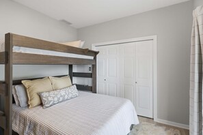 Una cama literera con estructura de madera, una puerta blanca y una alfombra de color claro.