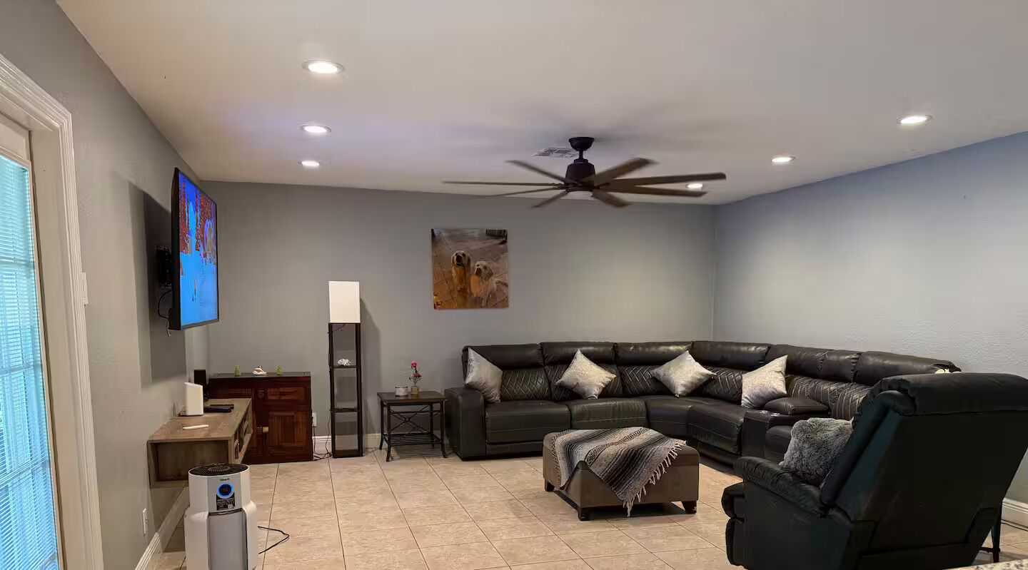 Ein Wohnzimmer mit einem Ecksofa, Deckenventilator, Einbauleuchten und einem flachbildfernseher an der Wand.