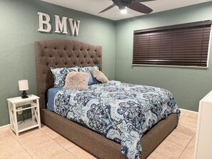 A bedroom with a tufted headboard, a patterned bedspread, a bedside table with a lamp, and a ceiling fan. - Welcome to your Private Lake Worth Oasis getaway! (Lake Worth)