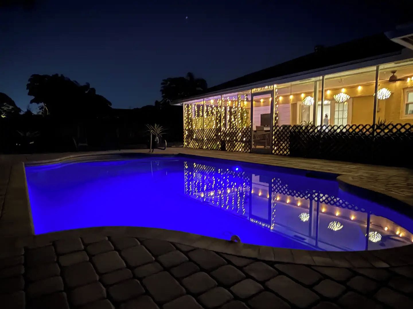 Une piscine dont le bord est illuminé de lumière bleue, entourée d’une allée dallée.