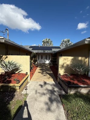 Un edificio residencial con acceso central, paneles solares en el techo y jardines ajardinados con acolchado rojo y plantas.
