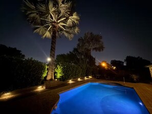 A nighttime pool area with a clear blue pool, surrounded by palm trees and illuminated by street lamps. - Welcome to your Private Lake Worth Oasis getaway! (Lake Worth)