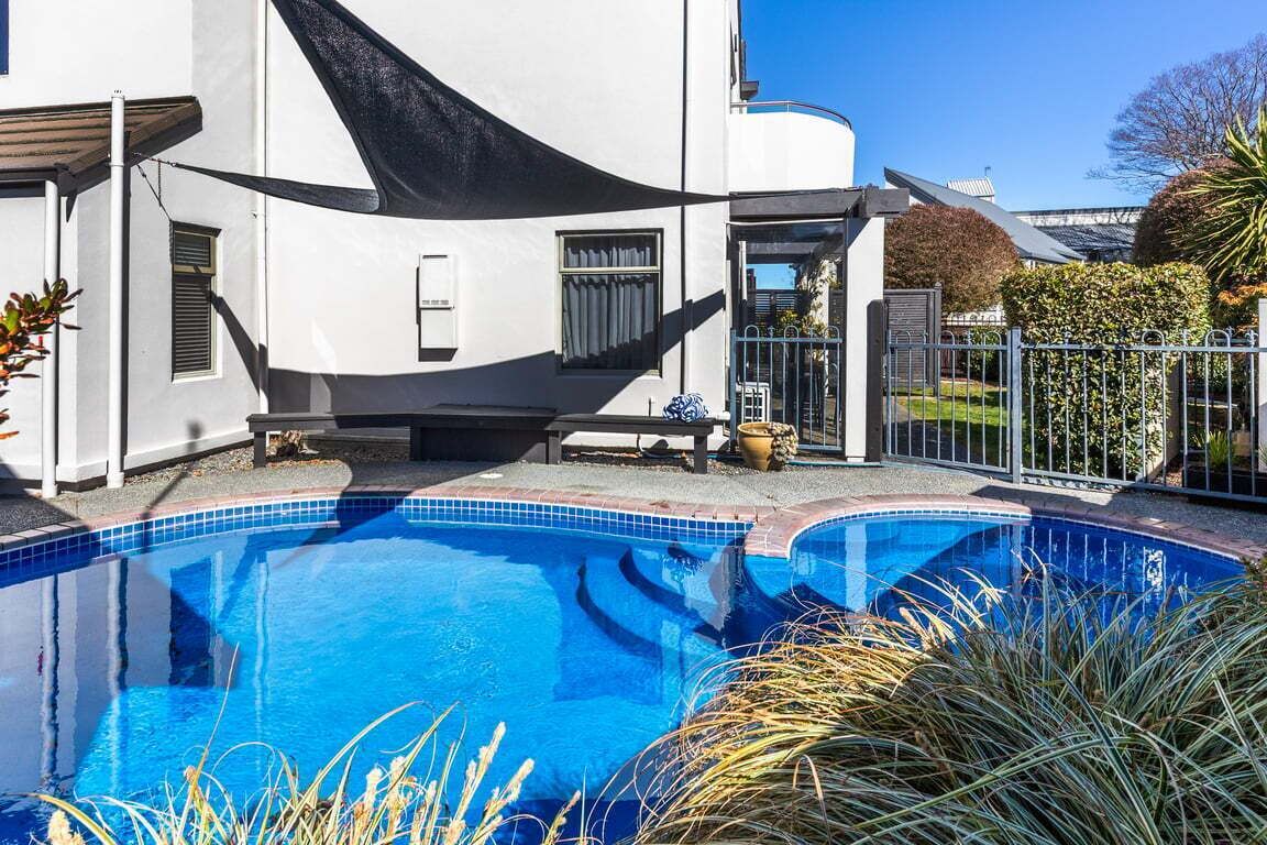 Une piscine avec un hamac, un bâtiment blanc et un jardin clos.