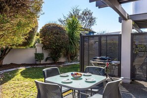 Eine Terrassengruppe im Freien mit Esstisch, Stühlen und einem Grillbereich im Hintergrund.