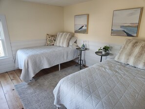 Ein Schlafzimmer mit zwei Betten, einem kleinen Tisch mit einer Pflanze und zwei Bildern an der Wand.