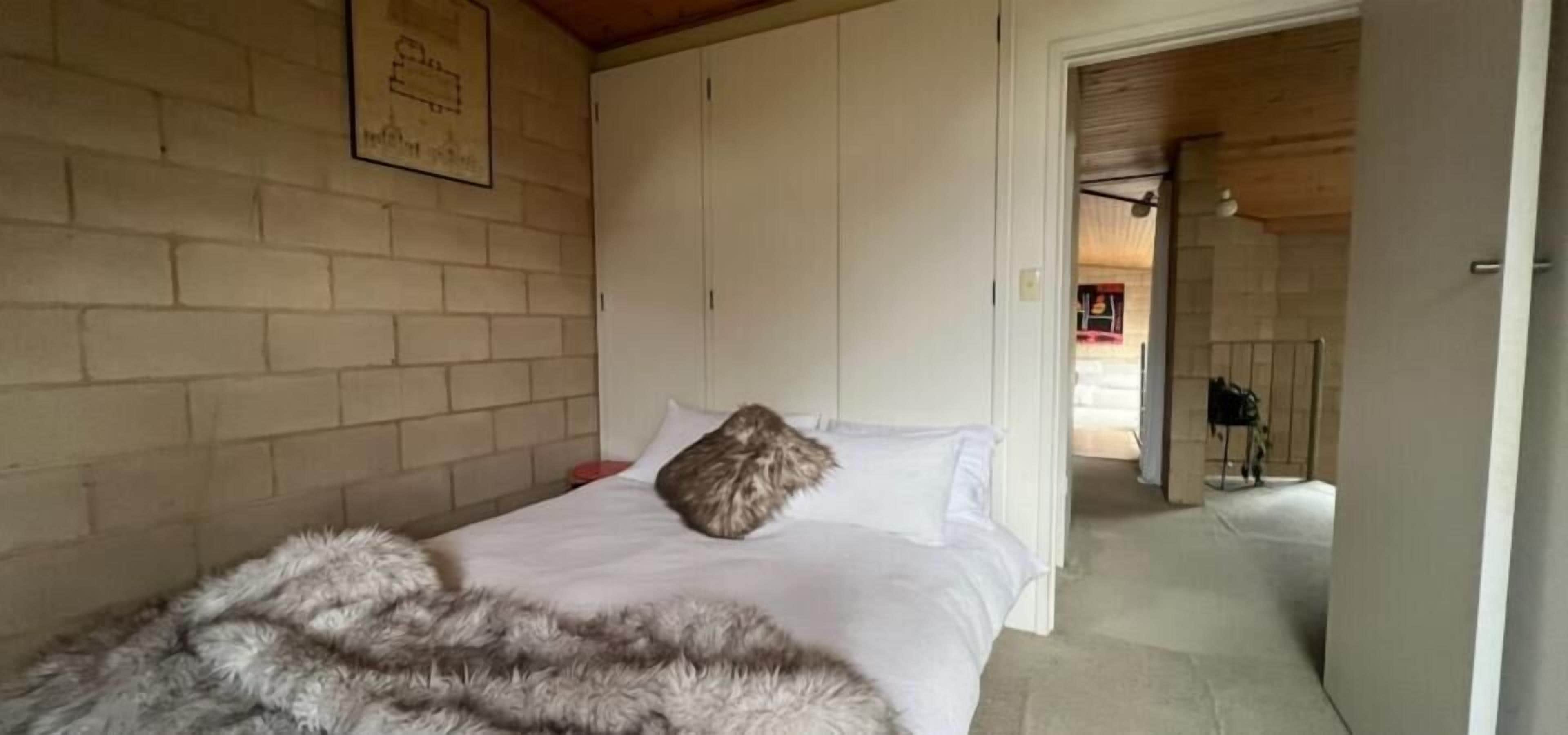 A bedroom with a bed, a fur throw, and a brick wall.