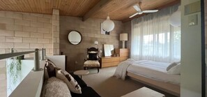 Une chambre à coucher comprenant un lit, une chaise, une commode, un miroir rond et un ventilateur de plafond.