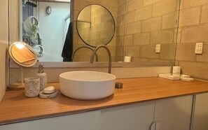 Une salle de bain avec un lavabo rond, un miroir et un plan de toilette en bois.