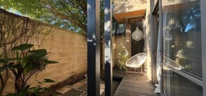 A modern outdoor space with a wooden deck, a glass door leading to a room, and a white chair. - Architectural Gem in Geelong (Greater Geelong)