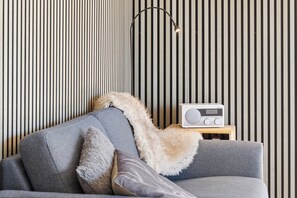A modern living room with a sofa, a fur throw, a radio, and a lamp against a striped wall. - Cozy holiday home with hot tub (Løgstør)